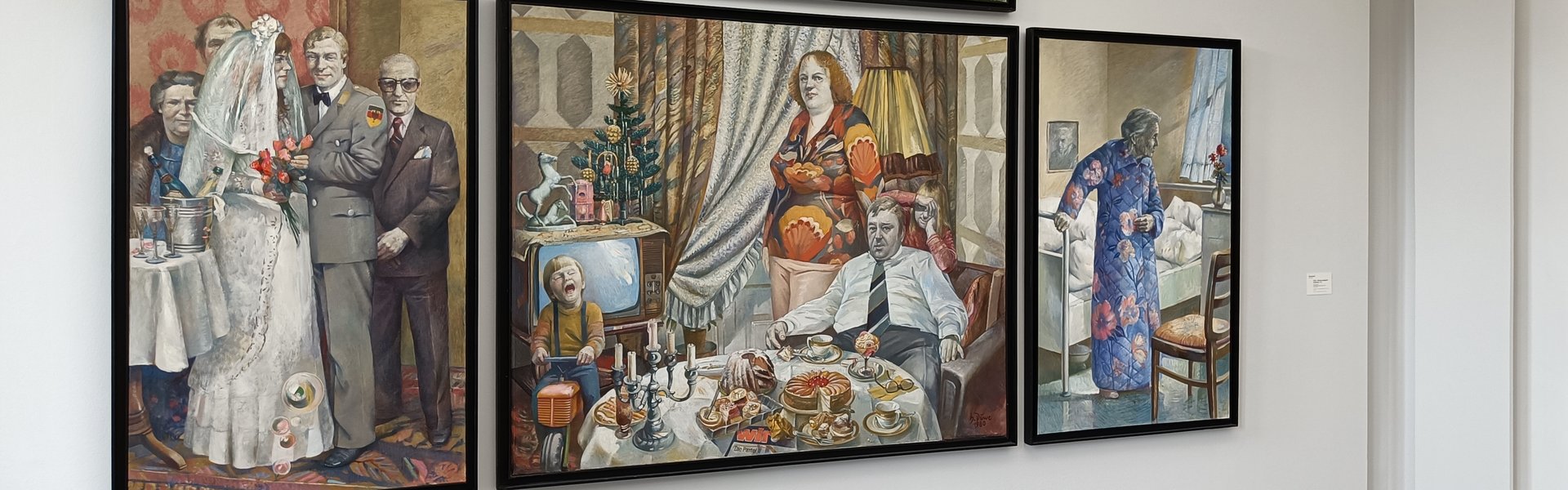 Eine bunte Fotografie. Darauf ist ein vierteiliges Kunstwerk zu erkennen. Auf dem obersten Abschnitt ist ein junger Mann und eine junge Frau zu sehen, die auf einer Picknickdecke liegen. Sie sind nackt. Im Hintergrund ist der Teil eines Autos zu sehen und ein oranger Sichtschutz. Darunter, auf dem linken Abschnitt, ist ein Brautpaar zu sehen. Die Frau trägt ein weißes Hochzeitskleid und der Mann trägt einen Anzug. Neben ihnen ist ein kleiner Tisch mit einem Sektkübel und Sektgläsern. Hinter dem Paar stehen drei weitere Personen. Die mittlere Leinwand zeigt ein Zimmer. Im Vordergrund ist ein reichlich gedeckter Esstisch. In der Mitte sind vier Personen zu sehen. Der Mann sitzt auf einem roten Sessel. Er trägt ein weißes Hemd und eine Krawatte. Hinter ihm, auf dem Sessel abgestützt, steht eine Frau in einer hellen Hose und einem reich verzierten Oberteil. Rechts hinter den beiden ist ein Mädchen zu sehen, das mit ihren Armen das Gesicht verdeckt. Links im Bild ist ein kleiner Junge auf einem Spielzeugtraktor. Er trägt ein oranges Oberteil und eine blaue Hose mit Hosenträgern. Im Hintergrund sind ein alter Röhrenfernseher und rechts daneben das Fenster mit langen Gardinen. Auf dem ganz rechten Teil des Vierteilers ist eine alte Dame zu sehen, die sich auf einem Krankenhausbett abstützt. Auf der rechten Seit im Hintergrund sieht man im Hintergrund ein geöffnetes Fenster, durch das Sonnenlicht flutet. 