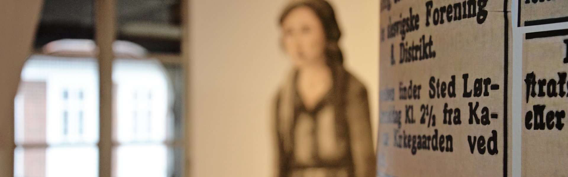 På farvefotografiet ses Oluf-Samson-Gangen. Udsigten fører direkte gennem gaden til havnen. Den venstre side af gaden er i sol, mens den højre side er i skygge. På den venstre side af gaden sidder letpåklædte kvinder på liggestole og soler sig. På den højre side sidder kun to kvinder. Længere bag i billedet arbejdes der på facaden af et af husene, mens en mand slentrer ned mod vandet.