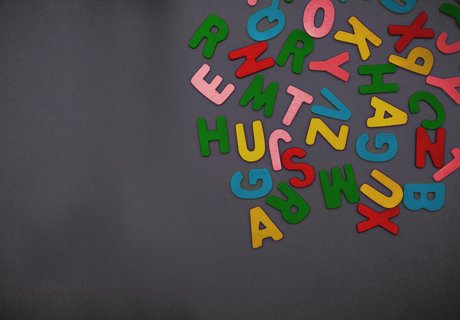 Farbige Holzbuchstaben liegen auf einem schwarzen Grund.