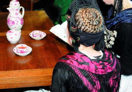 Es sind zwei Frauen in friesischer Tracht zu sehen, die Teetassen vor sich stehen haben.