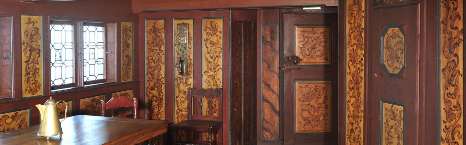 Der er træ med dekorationer på væggene og loftet i rummet. Der står en stol og et bord i rummet.