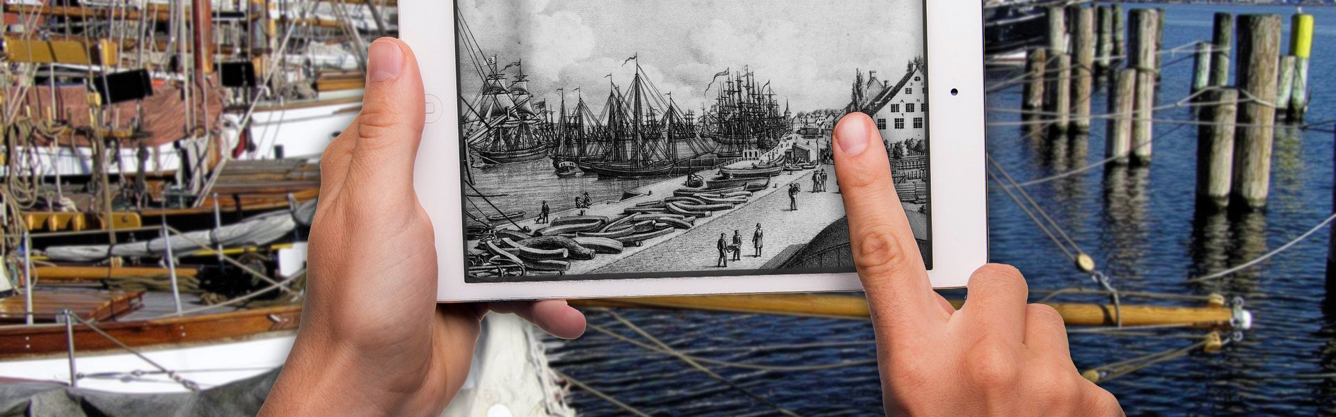  Im Vordergrund sind Hände zu sehen, die ein Tablet hochhalten und bedienen. Auf dem Tablet ist eine alte, gezeichnete Hafenansicht zu sehen. Im Hintergrund verschwommen ist der heutige Museumshafen zu sehen.