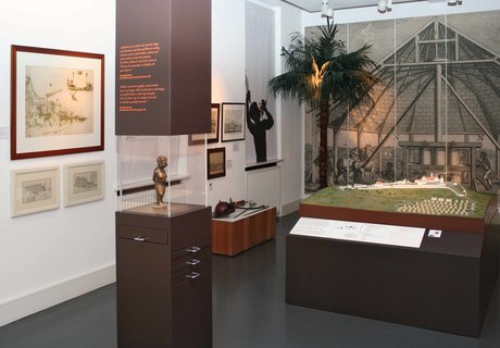 In der Mitte des Raumes steht eine braune Säule mit einer mittigen Glaseinfassung. Dort hinter ist eine Figur zu sehen, die einen versklavten Menschen aus Afrika darstellen soll. Dieser ist gefesselt. Dahinter steht ein großes Plantagenmodell mit kleinen Hütten und größeren Gebäuden für die Verarbeitung von Zuckerrohr. Im Hintergrund ist eine Wandtapete zu sehen. Auf dieser ist eine Zuckermühle abgebildet.