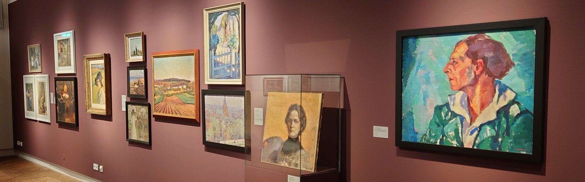 Es ist ein Raum zu sehen, in dem mehrere Bilder einer Ausstellung hängen.