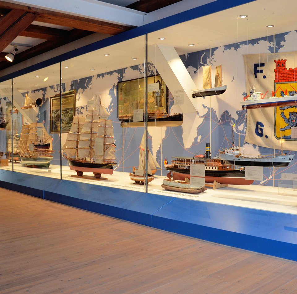 In der Ausstellung HAFEN & HÖFE gibt es eine ganz große Vitrine, die sich einmal über die gesamte Breite des Raumes zieht. In der Vitrine sind verschiedene Flensburger Schiffe zu sehen.