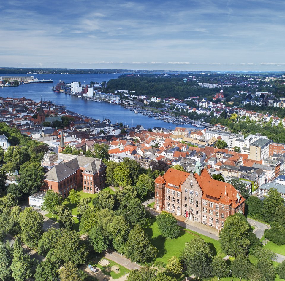 Die Luftaufnahme zeigt den Museumsbergmit seinen zwei Gebäuden im Vordergrund. Dahinter ist die Flensburger Förde und unzählige andere Gebäude zu sehen.