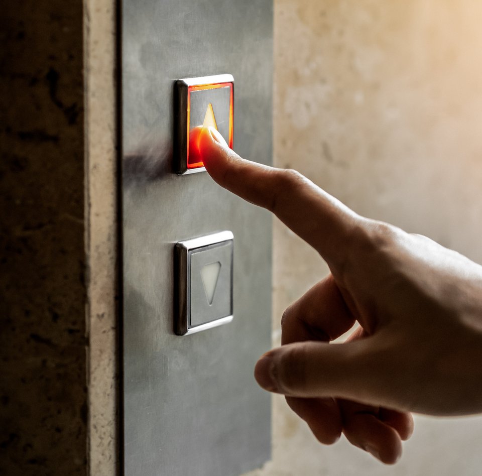 Nærbillede af en hånd, der trykker på en knap i en elevator.
