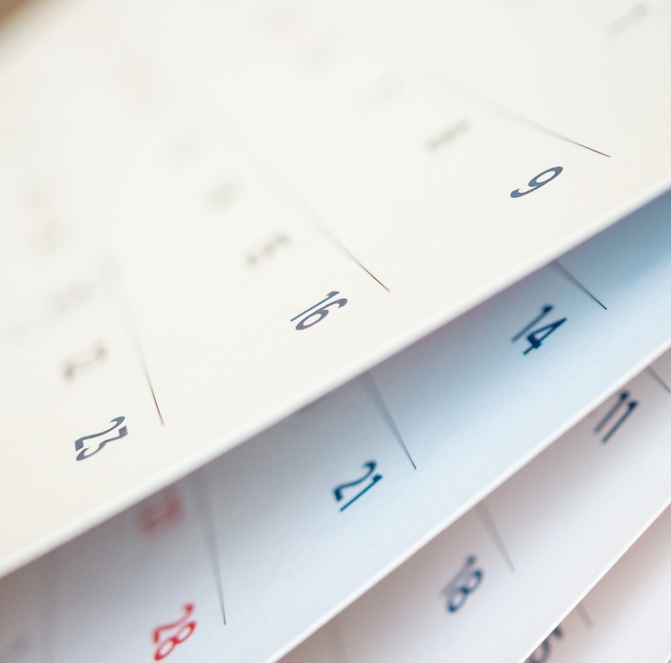 Nahaufnahme eine Kalenders. Es handelt sich bei dem Kalender um einen Wandkalender, der auf jeder Seite eine Monat anzeigt. Die Kalenderblätter sind leicht aufgefächert, sodass mehrere Monate erahnt werden können. 