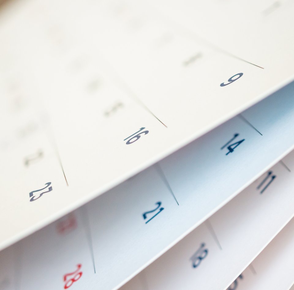 Nahaufnahme eine Kalenders. Es handelt sich bei dem Kalender um einen Wandkalender, der auf jeder Seite eine Monat anzeigt. Die Kalenderblätter sind leicht aufgefächert, sodass mehrere Monate erahnt werden können. 