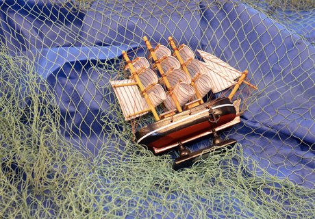Man sieht einen blauen Stoff. Darüber liegt ein grünes Fischer-Netz. Und ein Modell-Schiff liegt auf der Seite. 
