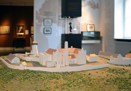 Det farvede fotografi viser en sukkerrørsplantage. Bagved ses en brun søjle med glas i midten. Bagved dette ses en træfigur, som er lagt i lænker. Bagved søjlen ses et kort, som er printet på væggen. Det viser trekantshandelen. Helt i baggrunden ses et andet rum med malerier af skibe og et portræt.