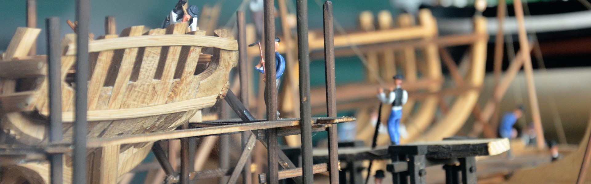 Nærbillede af en model, der viser, hvordan skibe blev bygget i gamle dage. I forgrunden ses skelettet af et sejlskib lavet af træ. I modellen er der placeret mange små figurer, der skal forestille arbejderne på skibsværftet. En af dem holder for eksempel en hammer i hånden.
