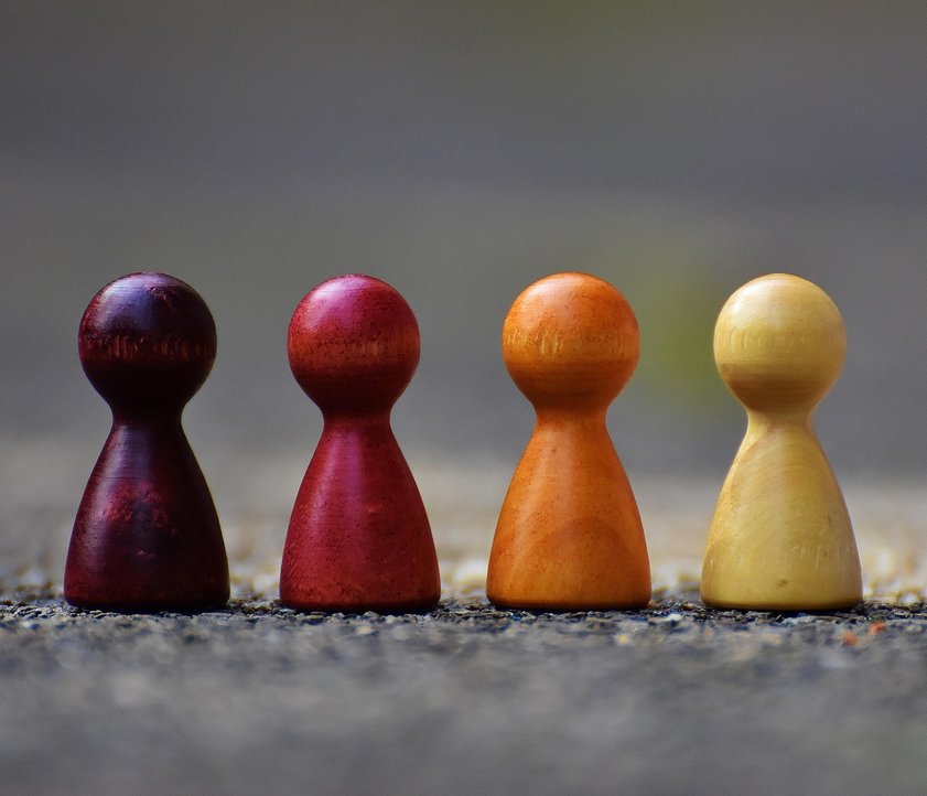 Auf dem Bild sind vier Spielfiguren zu sehen. Sie stehen alle nebeneinander in einer Reihe. Sie haben alle eine unterschiedliche Farbe. Sie stehen auf einer Straße. Jedoch ist sowohl der Vorder- als auch der Hintergrund sehr verschwommen.