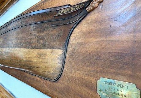 På en væg hænger et halvskib fra FSG. Det er et nærbillede.