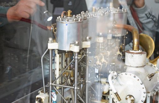 I forgrunden ses en model af en maskine. Modellen er udstillet i en vitrine. En frivillig fra teknikteamet peger med en lommelygte på en detalje på maskinen.