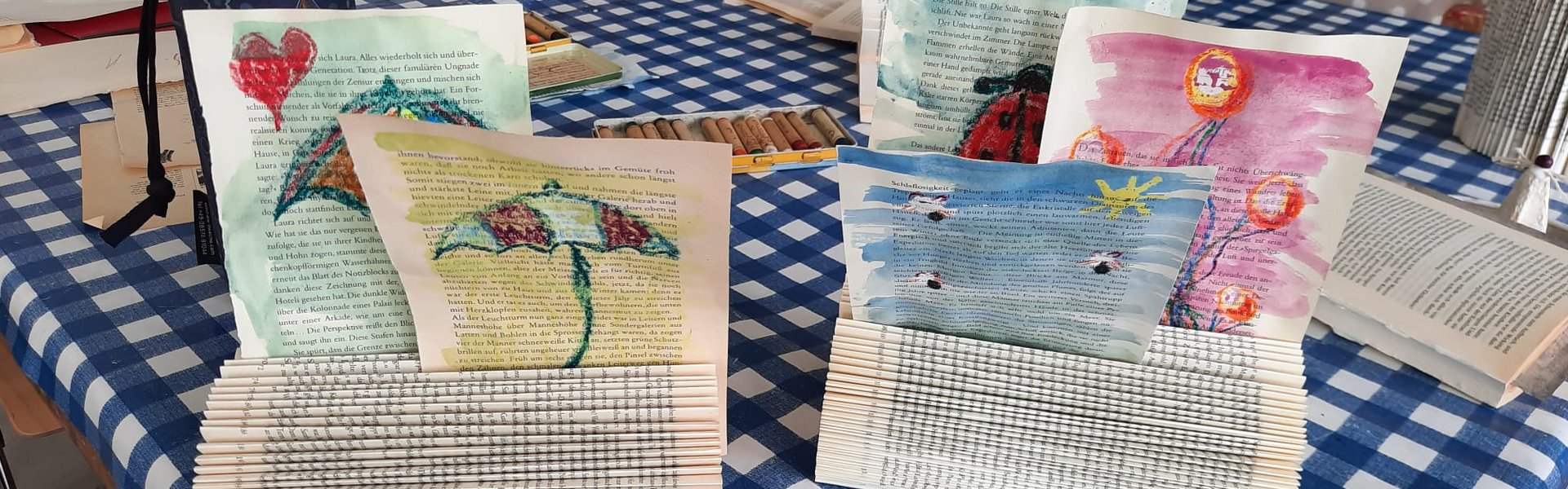 Das Foto zeigt die Ergebnisse einer Kreativwerkstatt. Es handelt sich um Zettelhalter aus Büchern mit selbst gestalteten, bunten Zeichnungen darin.