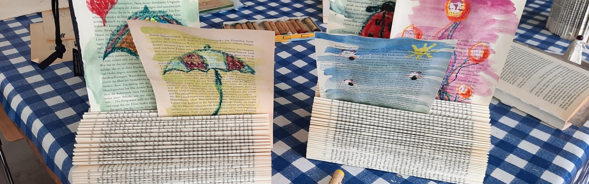 Das Foto zeigt die Ergebnisse einer Kreativwerkstatt. Es handelt sich um Zettelhalter aus Büchern mit selbst gestalteten, bunten Zeichnungen darin.