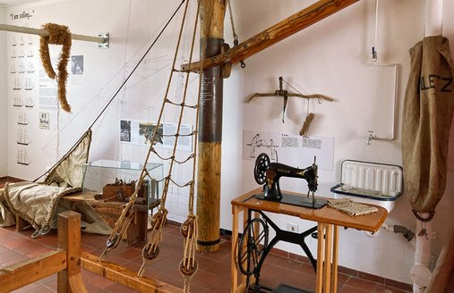 Man sieht eine alte Nähmaschine. Sie steht neben einem Mast. 