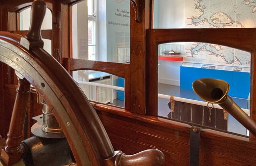 Billedet er taget fra HABICHT's styrehus. I forgrunden ses roret og til højre for det findes et talerør, der forbinder broen med maskinrummet. I baggrunden ses et søkort med stationer for Flensborgs fjordskibe.