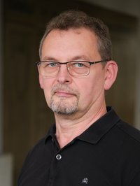 Portrait eines Mannes. Er trägt eine Brille und ein schwarzes Oberteil.