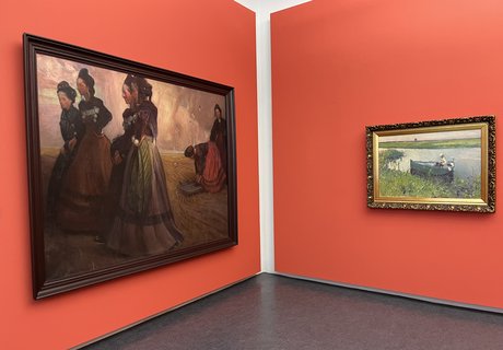 Das Foto zeigt zwei Gemälde in einem Ausstellungsraum. Die Bilder hängen vor einer roten Wand. Auf dem rechten Gemälde sind sechs Frauen abgebildet. Alle tragen Tracht. In der rechten Bildhälfte befinden sich vier Frauen. Sie stehen als Gruppe zusammen. Links etwas weiter hinten hocken zwei Frauen. Auf dem anderen Gemälde ist ein Mann in einem kleinen Ruderboot abgebildet. Er hat eine Angel in der Hand.